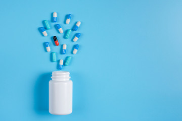 Blue and white pills, tablets and white bottle on blue background