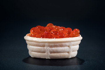 Tartlet with red caviar on a black background. Structure of caviar of a salmon, cold appetizers.