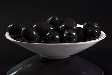 Dish of the canned black olives on a black background.