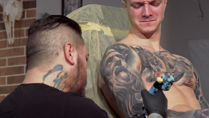 Young man getting painful tattoo on his arm. Sliding cropped shot of a male customer getting tattooed at workshop. Rear view shot of professional tattoo artist working