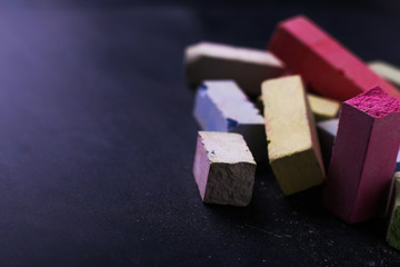 Multicolored crayons lie on a black chalkboard, copy space, macro. The concept of school, education and childhood.