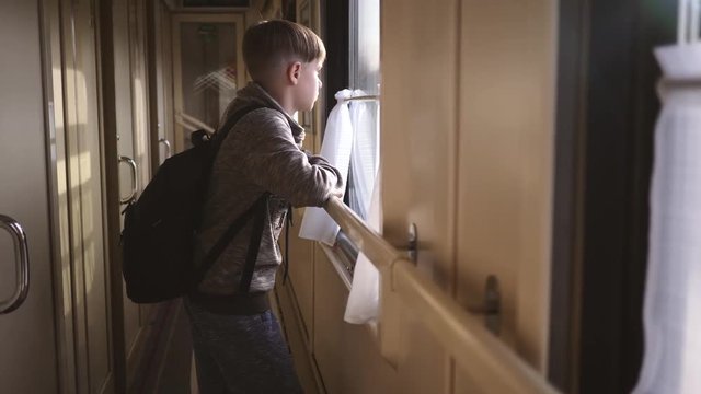 The boy stands at the train window and looks out the window at the running landscapes. Travel by train. Tourism on vacation, travel around the world.
