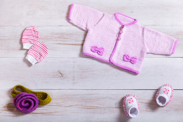 Baby clothes pink knitted tiny sweater cotton little mittens socks on white wooden background, infant cloth set on table, child newborn fashion clothing for girl, modern kid apparel shop, top view