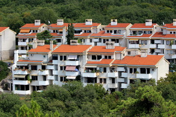Closely built attached apartment building with few floors and multiple balconies completely surrounded with dense forest vegetation on warm sunny day