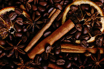 Obraz na płótnie Canvas Cinnamon sticks, star anise, coffee beans and dried orange on the kitchen table. Fragrant spices for coffee drink, close-up.