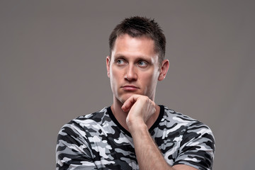 Obraz premium Moody portrait of pensive thoughtful man looking away thinking with hand on chin on gray background. 