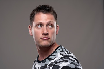 Obraz premium Handsome young adult man in army shirt looking back over the shoulder at copy space on gray background. 