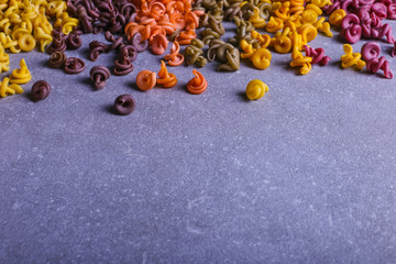 Fototapeta na wymiar Multicolored pasta of unusual shape with natural vegetable dyes, scattered on the table. Background closeup.