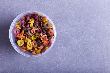 Multicolored pasta with the addition of natural vegetable dye. In a jar on a concrete table. Top view, copy Space.