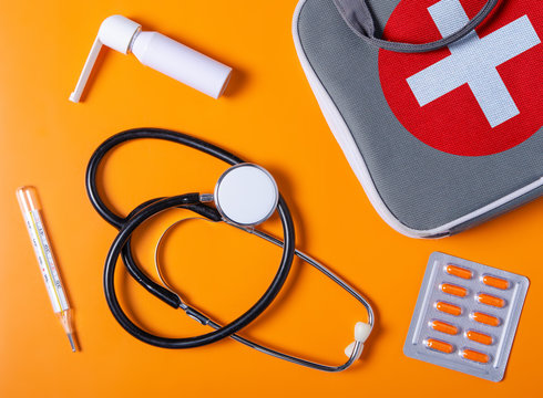 Flat lay composition with first aid kit, stethoscope, thermometer, throat spray, blister capsule on color orange white on background, flat lay, top view