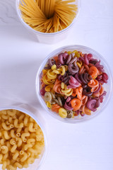 Multicolored pasta with the addition of natural vegetable dye. In a jar on a white table. Top view, copy Space.