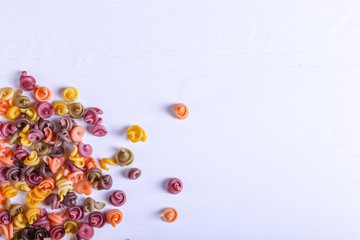 Multicolored pasta with the addition of natural vegetable dye. Scattered on a white table. Top view, copy space.