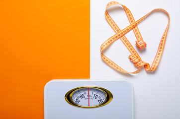bathroom weigh scale and measuring tape on color white orange background, flat lay, top view