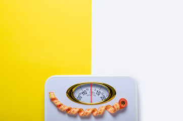 bathroom weigh scale and measuring tape on color white yellow background, flat lay, top view