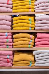 Neatly folded clothes. Rack of clothes with warm. Wooden cabinet with a stack of sweaters. Coloured clothing. Neat stacks of folded clothing on the shop shelves. vertical photo