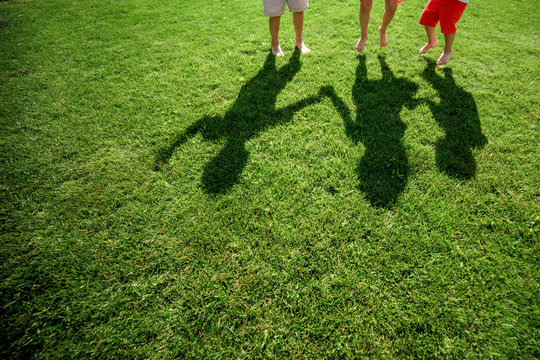 Kids with their shadows on grass. silhouettes of three persons standing with their hands stretched up