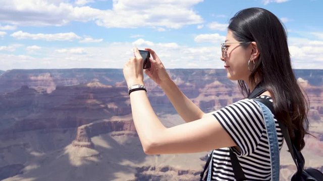 self guided hiking trip in summer. asian exchange student taking photo of beautiful desert mountains with smart phone on vacation nature wild travel. Blue sky with clouds in Grand Canyon National.