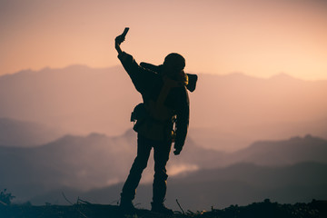 Silhouette of traveler with backpack standing take photo on the mountain. travel concept.