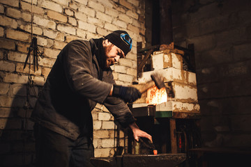 The blacksmith manually forging the red-hot metal on the anvil.