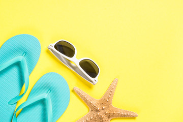 Blue flip flops, sunglasses and starfish on yellow top view.