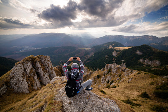 Hiker sitting on top of mountain and making picture with mobile phone  