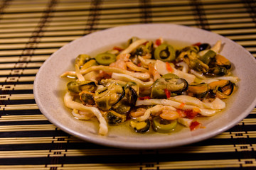 Ceramic plate with different sea food and olives on a bamboo mat