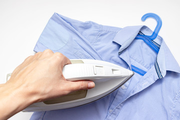 Fototapeta premium Woman hand holding a modern electrical white iron, a blue shirt on background, close up view - ironing, laundry and housework concept