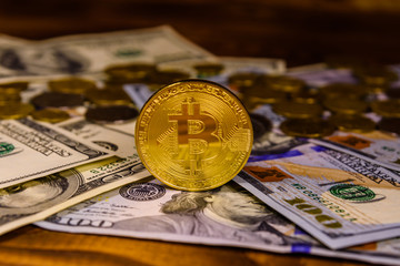 Bitcoins and one hundred dollar bills on wooden table