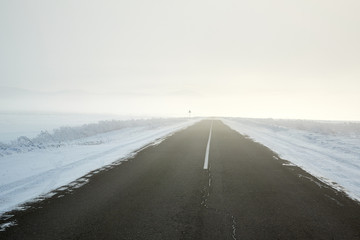 view of empty road with snow covered landscape while snowing in winter season.