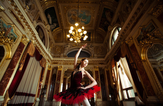Beautiful ballerina dancing in a luxurious hall in a red dress.