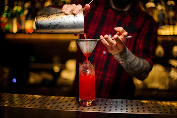 Fototapeta na wymiar Bartender pouring a Hurricane Punch cocktail from the steel shaker through the strainer