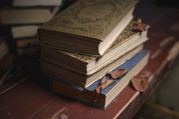 Obraz premium a stack of old vintage books on a red wooden table and dry leaves