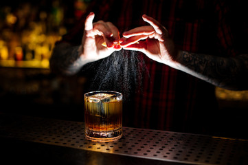 Professional bartender in red shirt adding orange zest juice to a Rusty Nail cocktail