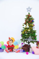 Baby in a christmas dress  sitting next to a decorated christmas tree