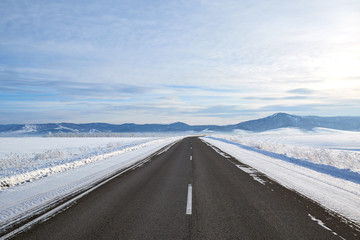 scenic view of empty road with snow covered landscape while snowing in winter season. Blue sky On the horizon.