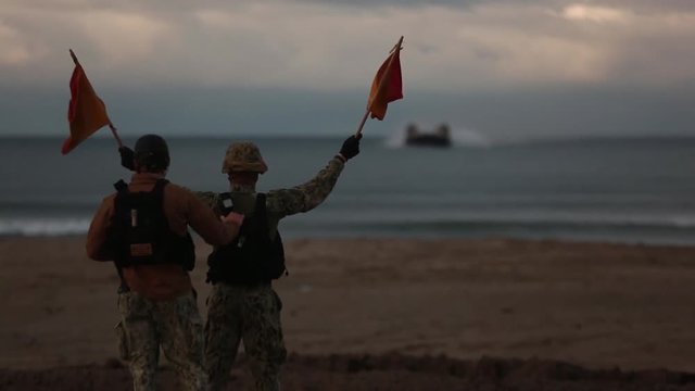 Soldier holding signal flags for amphibious vehicle arrival at beach