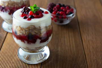 Glass jar withovernight oats, granola and yogurt with berry, raspberries and blackberries on wooden cutting board over wooden background. Healthy food.
