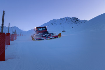 Snow grooming machine preparing a ski slope in twilight. Winter ski resort La Plagne in French Alps