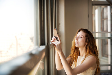 Portrait of young woman taking photo trough window 