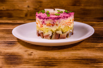 White plate with russian traditional new year salad herring under fur coat on wooden table