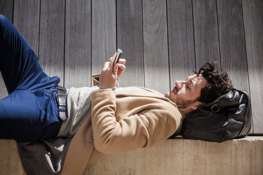 Side-view of man texting on ledge 