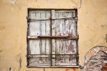 Closed window with wooden planks on old wall.