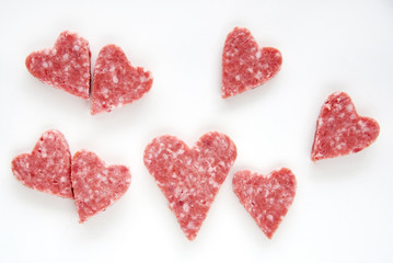 Obraz na płótnie Canvas Salami sausage sliced into heart-shaped pieces on a white background
