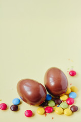 Chocolate Easter eggs and sweets on pastel yellow background