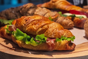 Photo of tasty and fresh croissant sandwich with salad, ham, cheese, tomatoes. Morning breakfast concept. Healthy and fast food