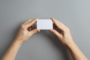 Hands holding a blank card or a ticket/flyer on gray background