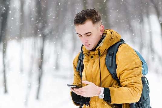 Tourist guy typing mesage while walking in the winter cold forest