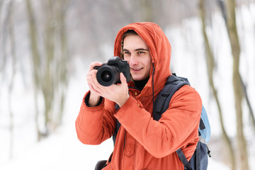 Fototapeta na wymiar Blonde photograph boy in the hood standing with camera on the winter forest background
