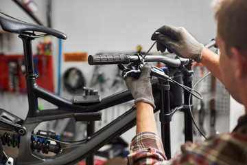 Cropped shot of male mechanic working in bicycle repair shop, serviceman repairing modern bike...