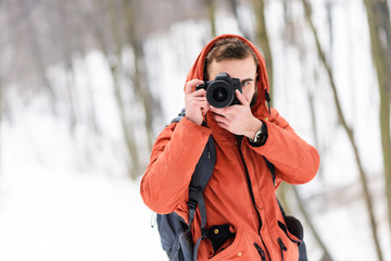 Blonde photograph boy in the hood shooting winter trees with snow while walking in the forest